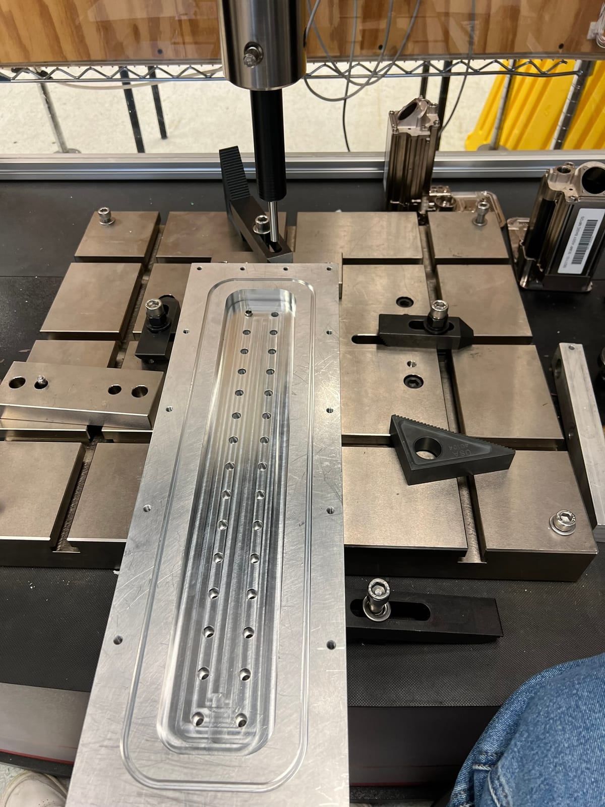 A machined aluminum manifold that ports high-pressure gas to twenty pressure-relief valves, fixtured on a mill.
