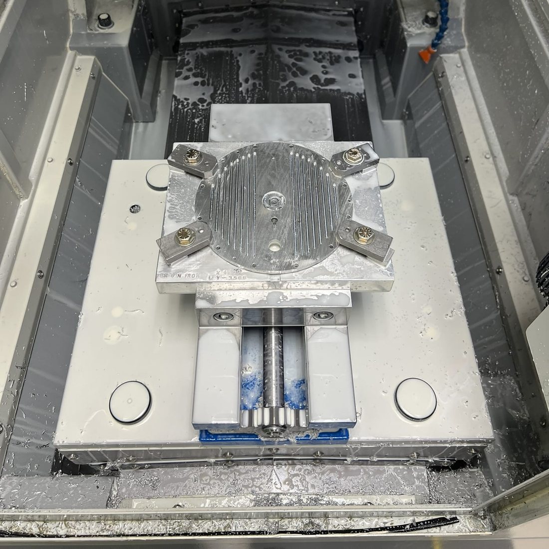 The finned top plate being machined on a CNC mill, clamped with soft jaws under coolant.