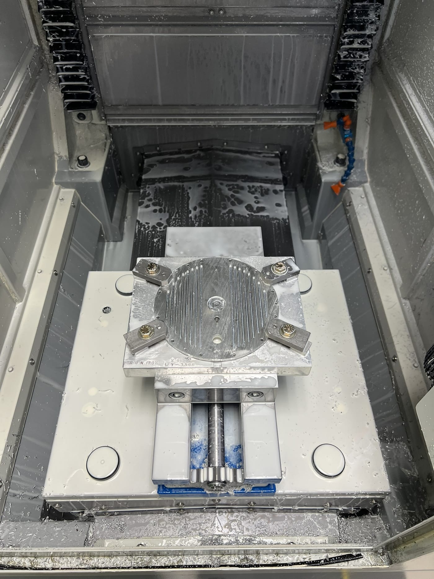 The finned top plate being machined on a CNC mill, clamped with soft jaws under coolant.